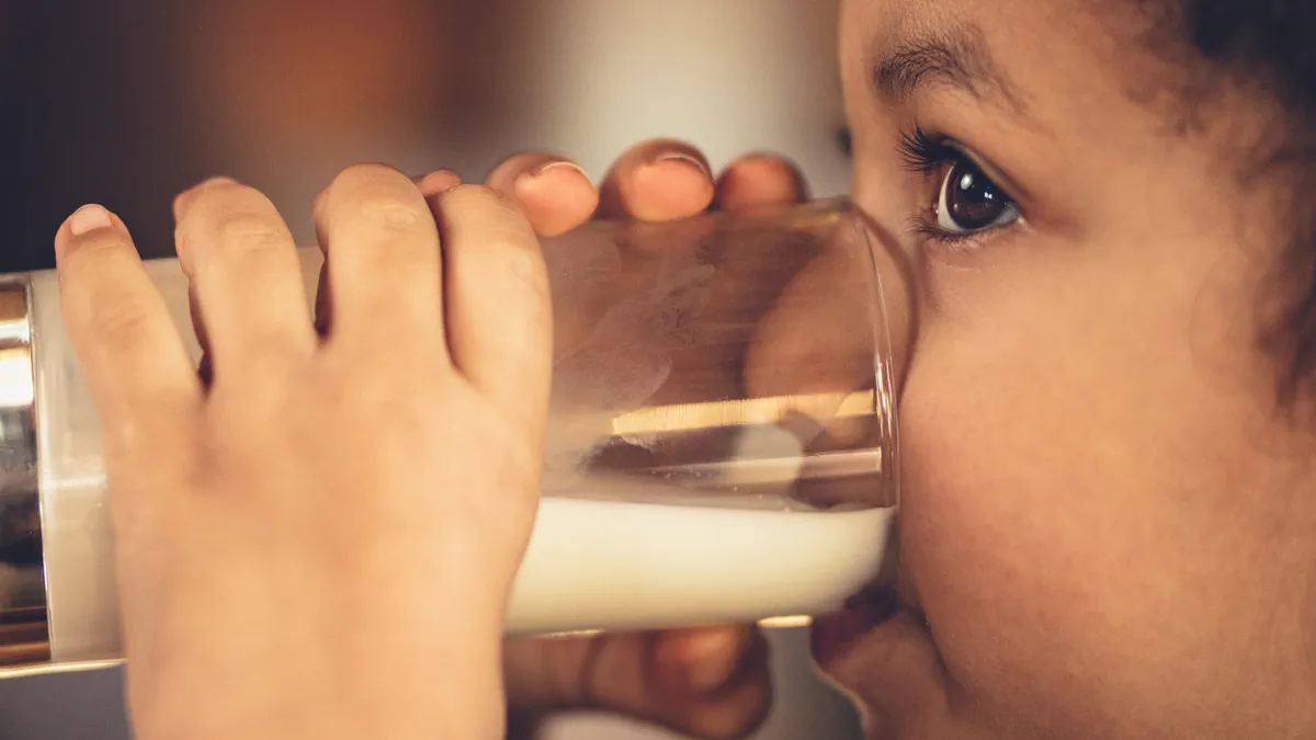 A young child drinks a glass of milk.