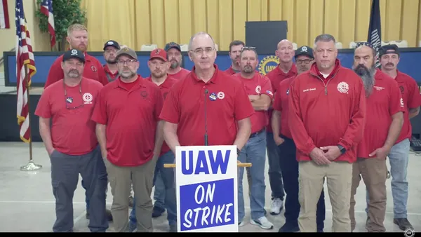 Fourteen people in red shirts, with one standing behind a podium.