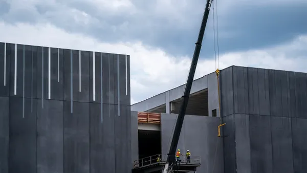 Two members of a construction crew work on a gray, monolithic structure.