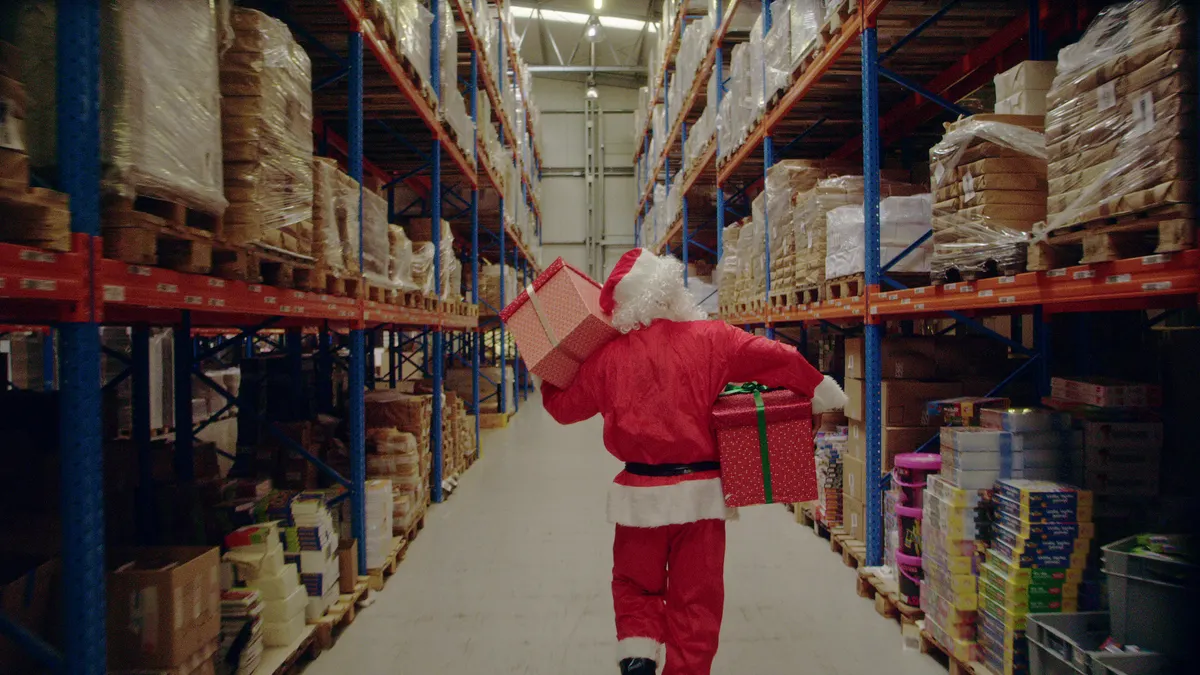 Santa in a warehouse picking up Christmas gifts.