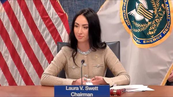 A woman sits at a desk in front of two flags.