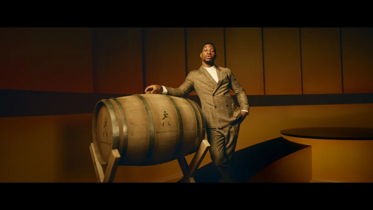 Actor Jonathan Majors rests his arm atop a barrel of Johnnie Walker.