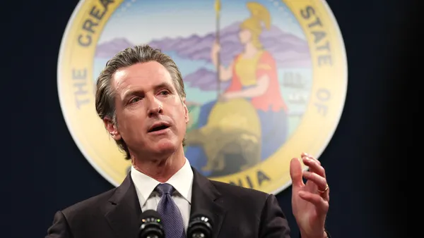 A person in a suit speaks in front of a seal for the state of California.