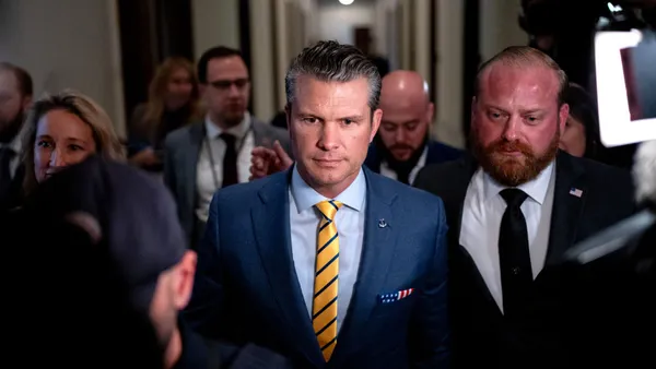 Man in blue suit and yellow tie walks through a crowded hallway