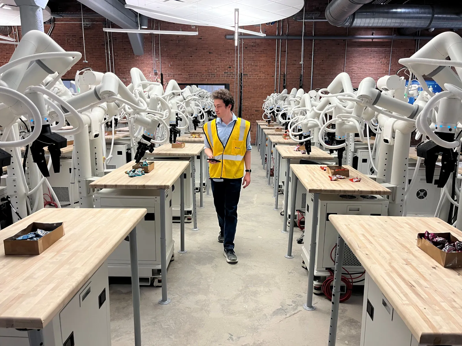 A Tutor Intelligence employee walks between a row of robots, inspecting the machines to ensure they operate correctly.