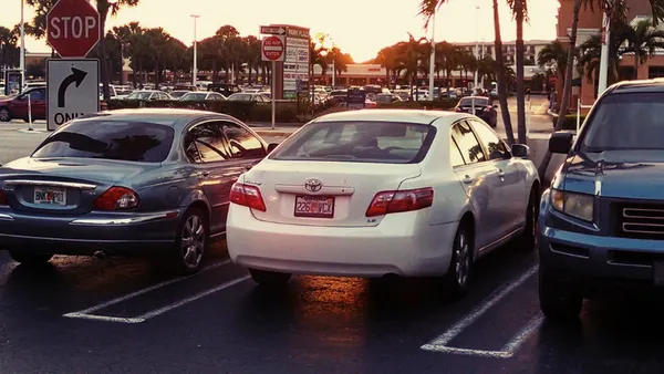 A row of cars parked in a parking lot outside of a shopping center.