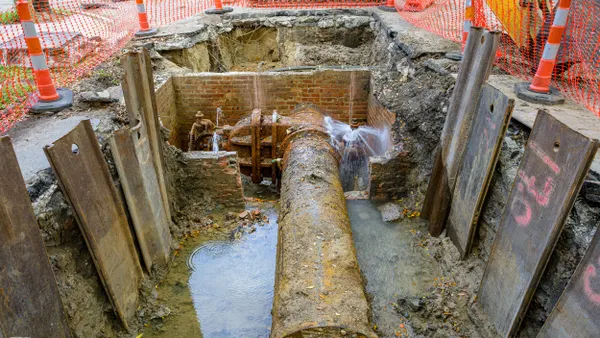 Broken, rusty and crusted water pipes in a deep concrete trench.