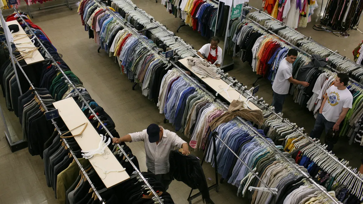 An aerial view of people shopping at a thrift store. They are looking through ailes of shirts.