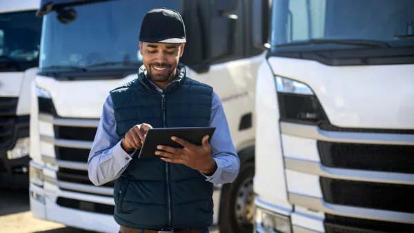 A person uses a tablet near parked trucks.