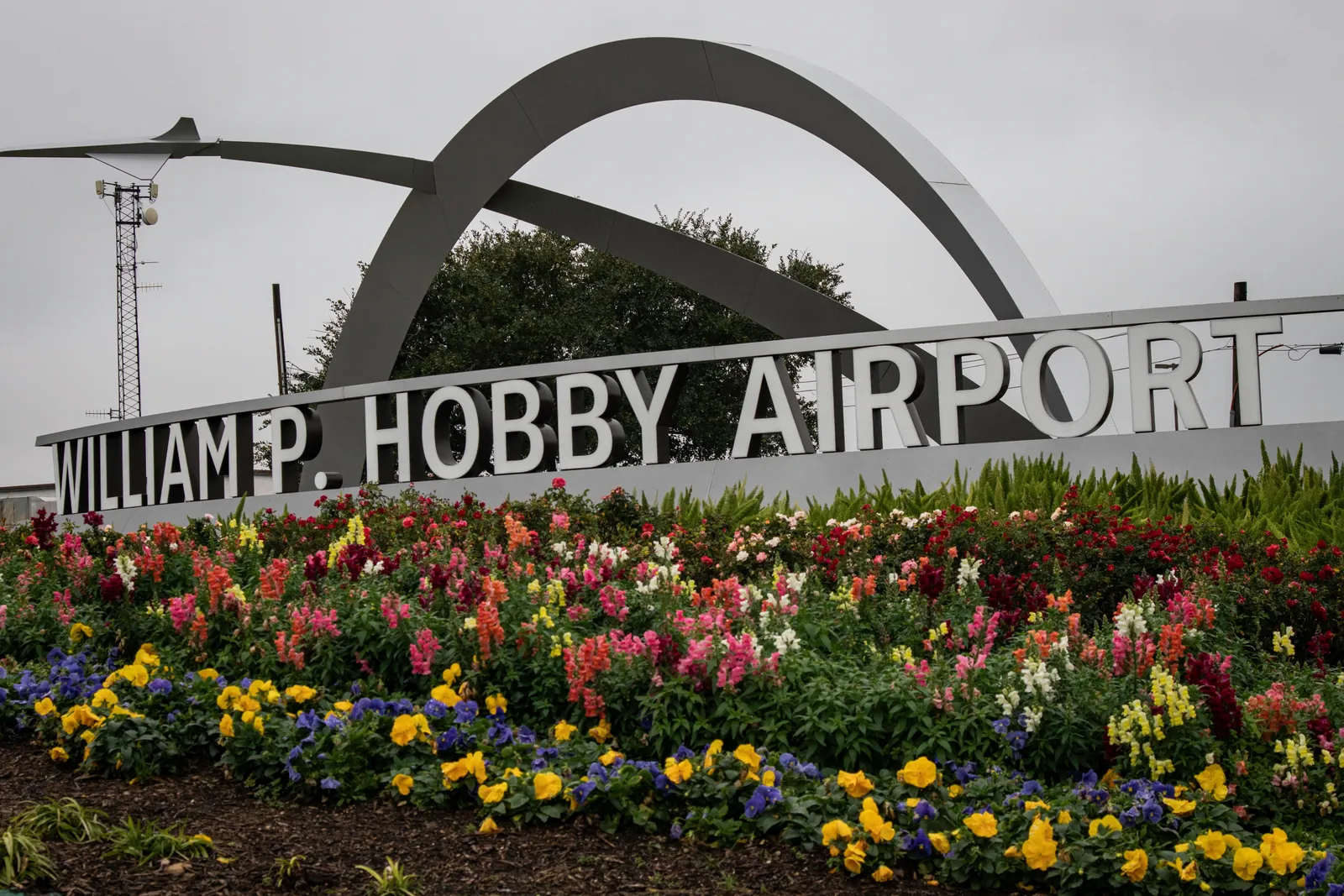 Signage amid grass and a bright sky reads &quot;William P. Hobby Airport&quot; with a metal arch in the background.