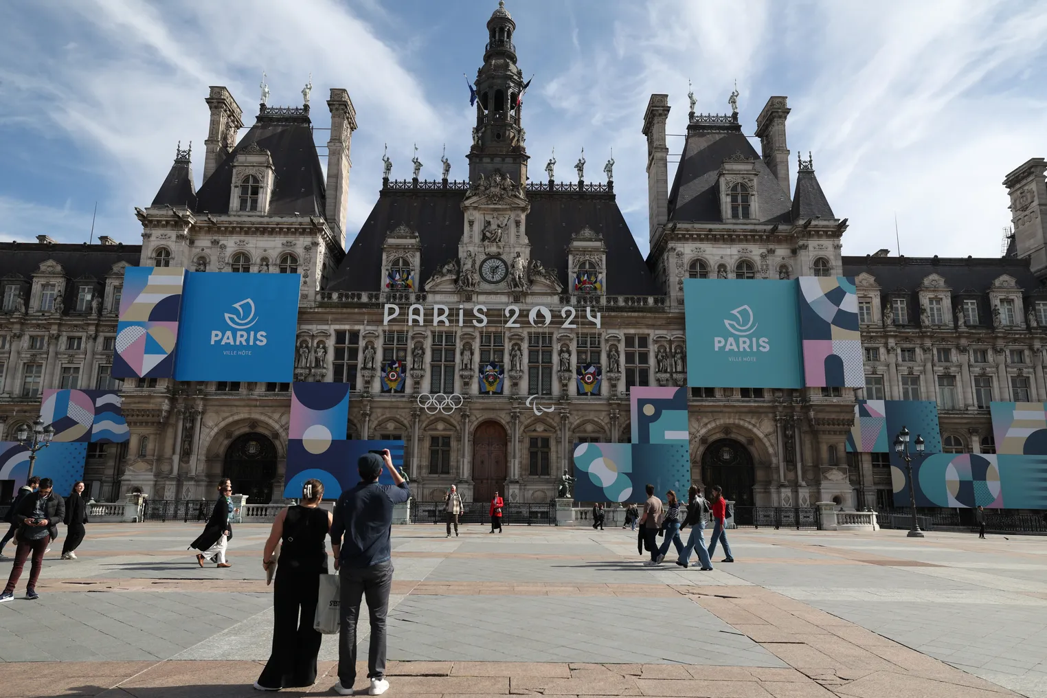 Paris town hall draped with the city's 2024 Olympic logo and a plaza with people.