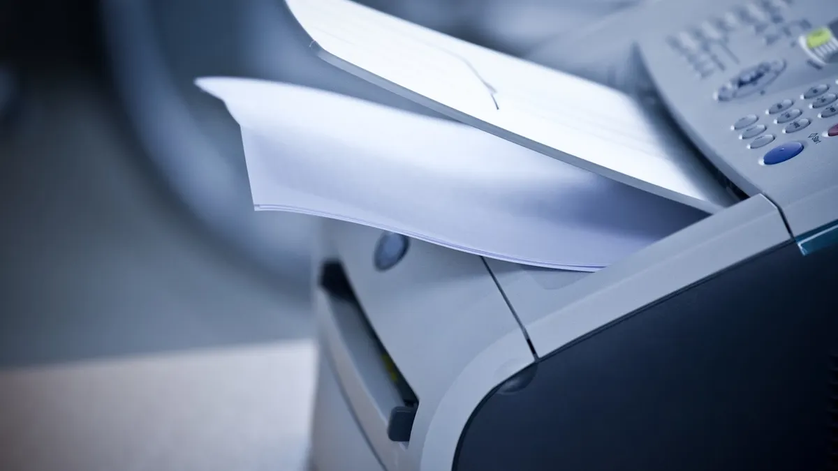 A laser printer with printed documents sits unattended in an office.