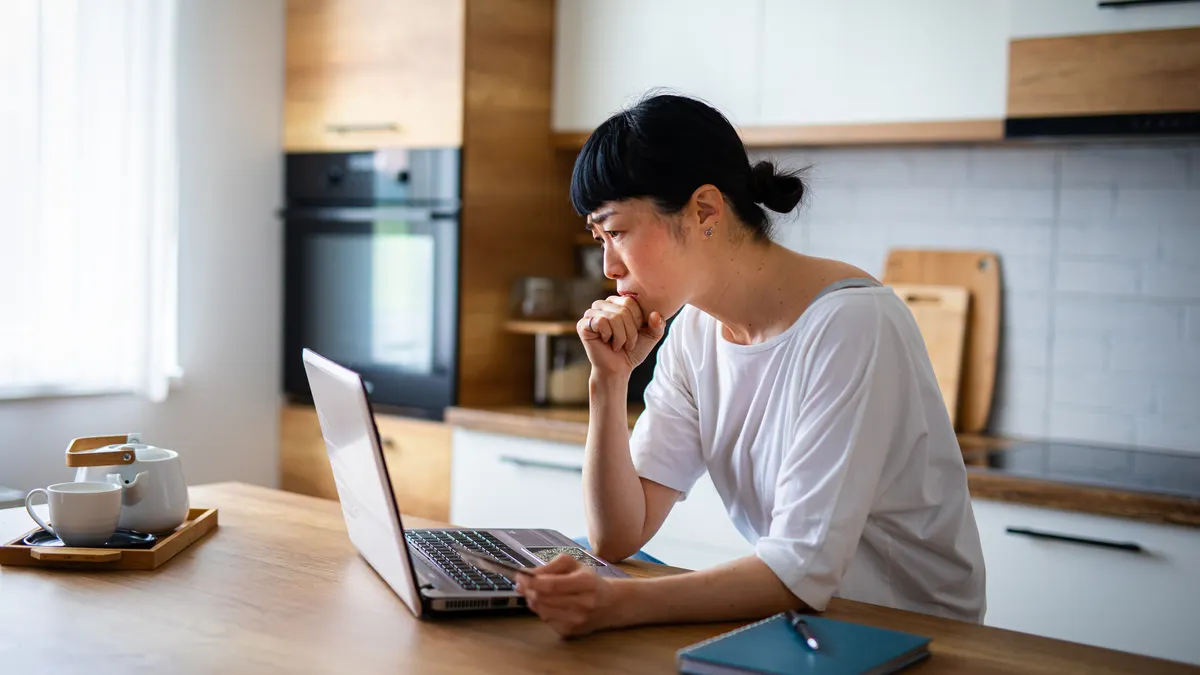 Customer looks at laptop computer with a credit card in hand looking concerned.