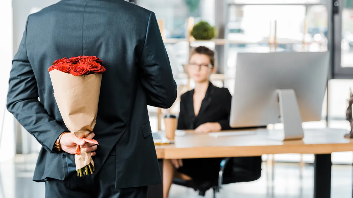 cropped image of businessman hiding bouquet of roses behind back to surprise businesswoman in office