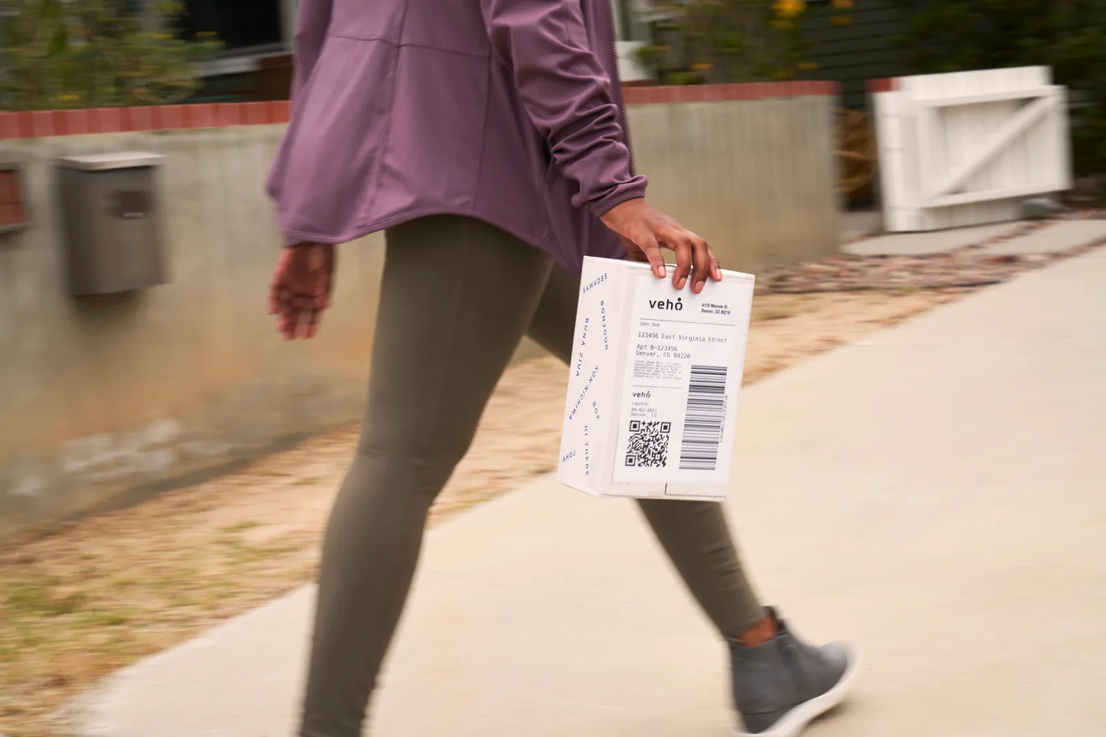 A person carries a package. The package reads, "Veho."