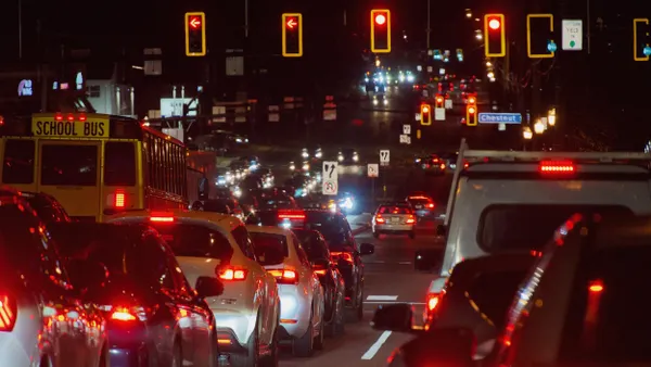 Night scense of a multilane road filled with cars and a school bus stopped at a red light.