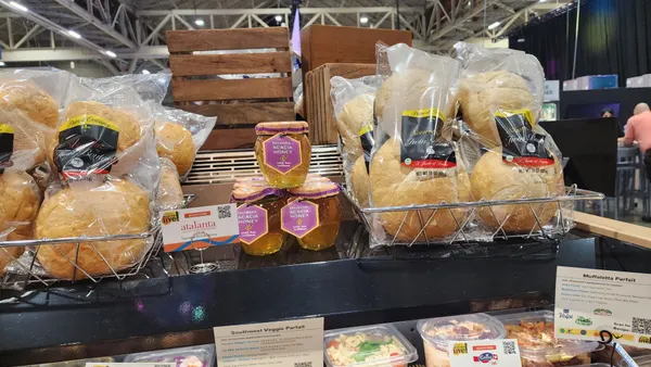 Bakery display in a store; baskets of packaged bread and jars of golden fig honey are arranged neatly, surrounded by salads in clear containers below.