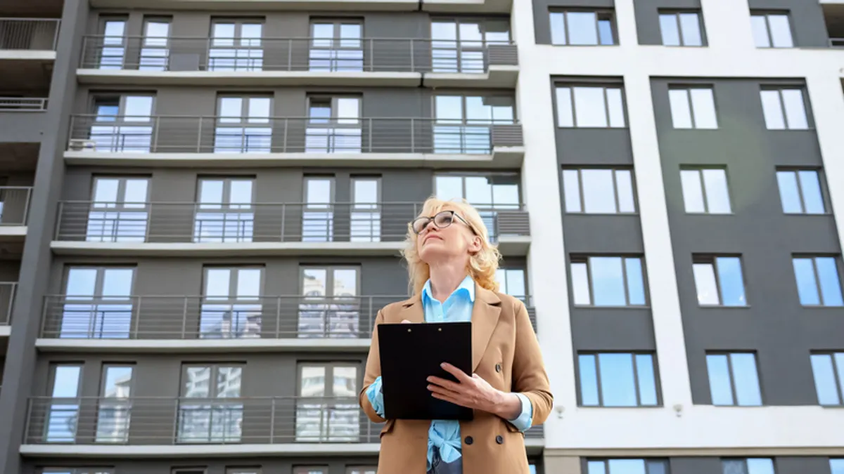 Woman making notes on clipboard with apartment building in the background.