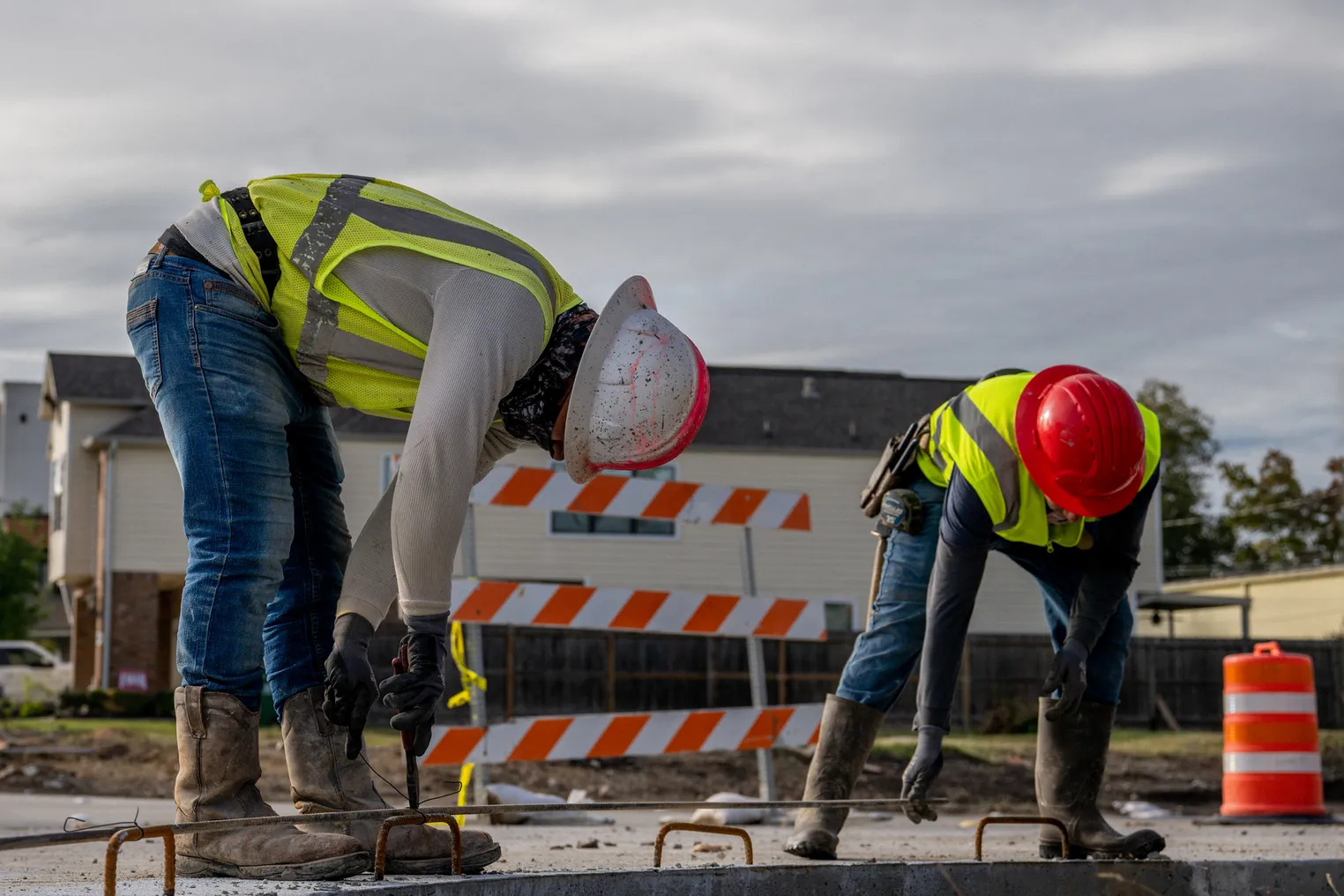 Two construction workers bend over to perform work.