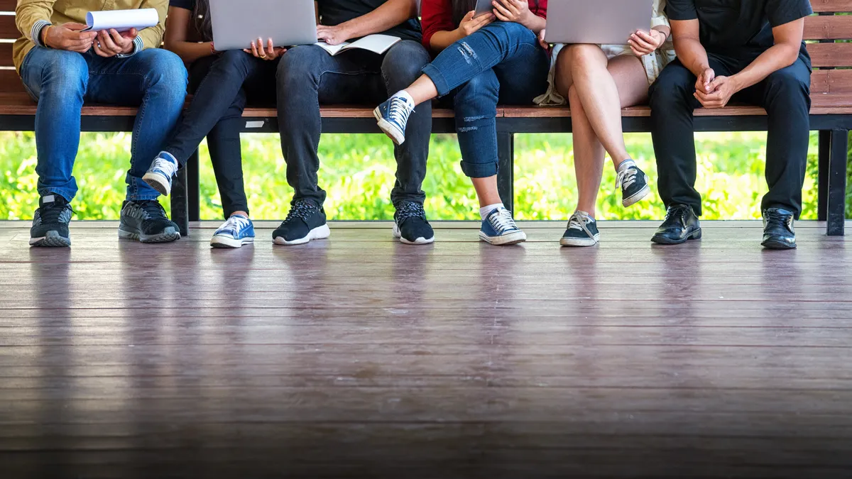 A row of people sitting on a bench, only visible from the waist down.