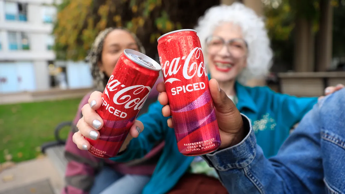 A close-up of two people holding cans of Coca-Cola Spiced