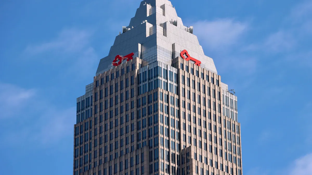 Low-angle view of a tall glass and steel skyscraper with a stepped Art Deco-style crown. A large red key is at the top of the building under a clear blue sky. 