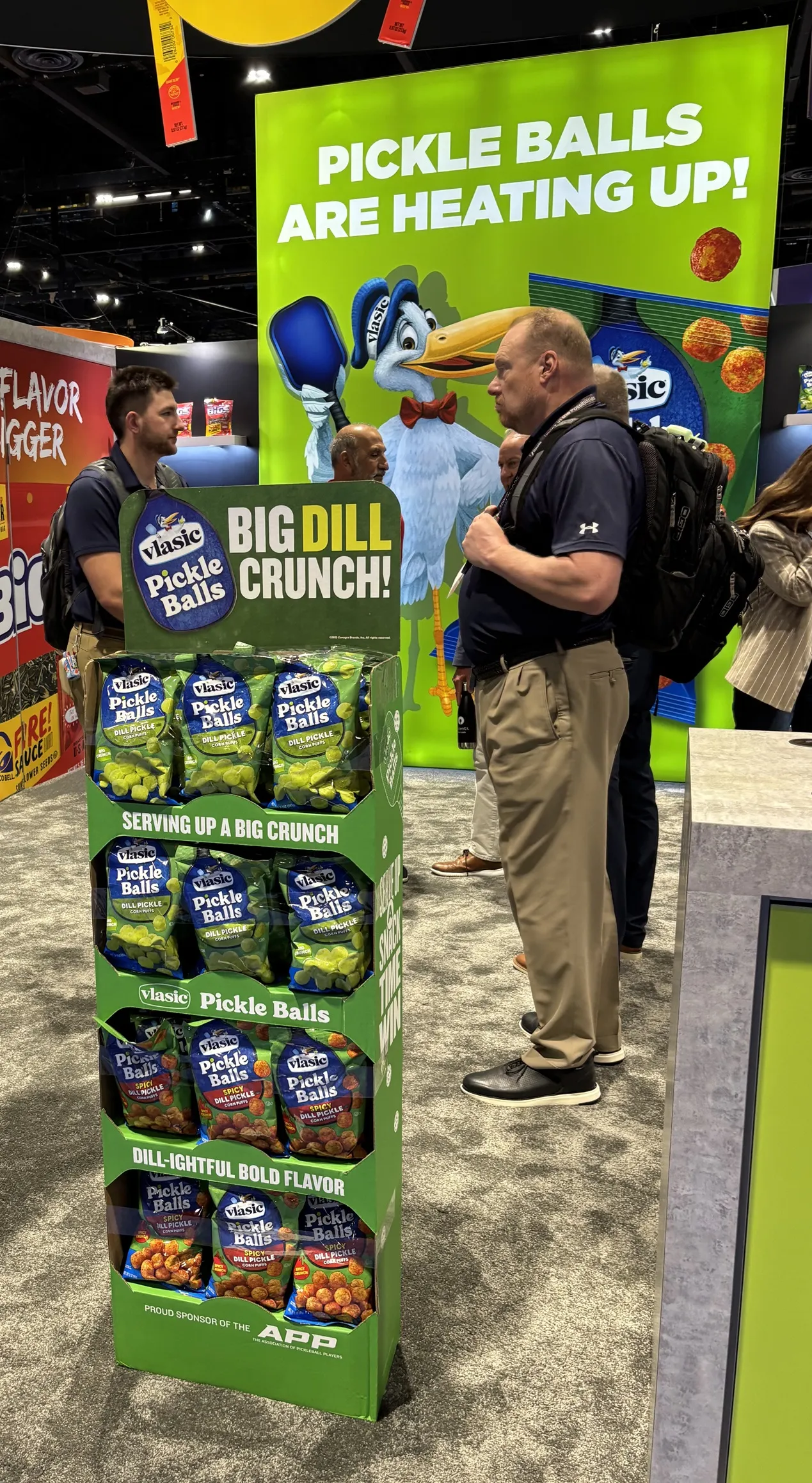 A photo of a display of bags of salty snacks. The bags say "Vlasic pickle balls" and a sign in the background says "pickle balls are heating up."