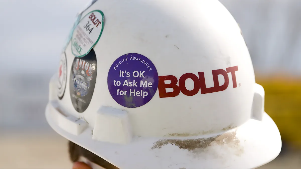 A white Boldt construction hard hat with a circular sticker that reads "Suicide Awareness It's OK to Ask Me for Help"