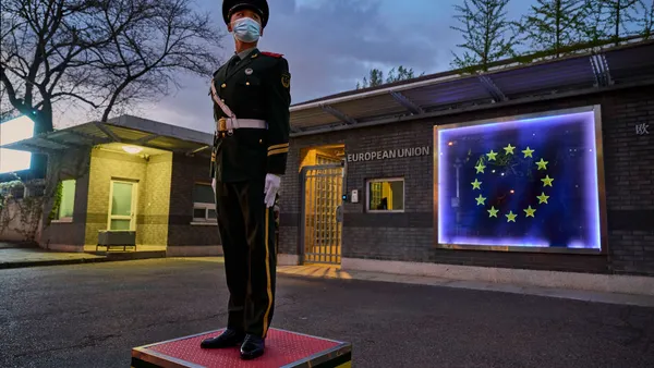 A member of the Peoples Armed Police stands guard in front of the flag of the European Union displayed on the side of a building.