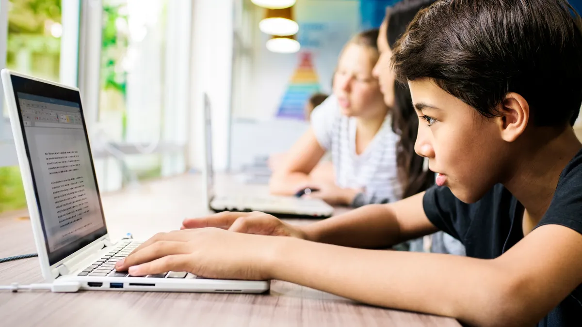 A students is seen from the side, sitting at a table with an open laptop.