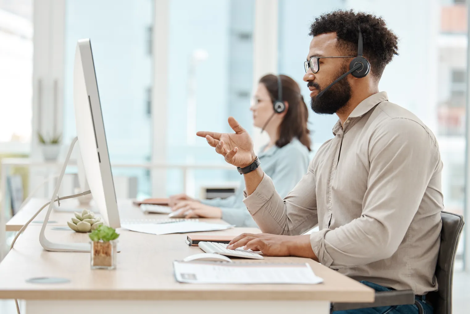 Picture of a man and a woman working at two computer stations in an office with headsets on.