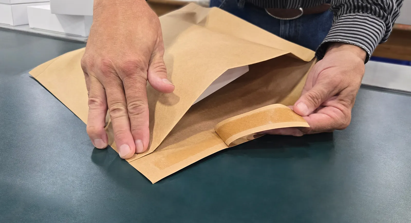 A person's hands are seen pulling a seal strip on a paper-based mailer.