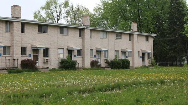 Older white-brick apartments with unkempt lawn.