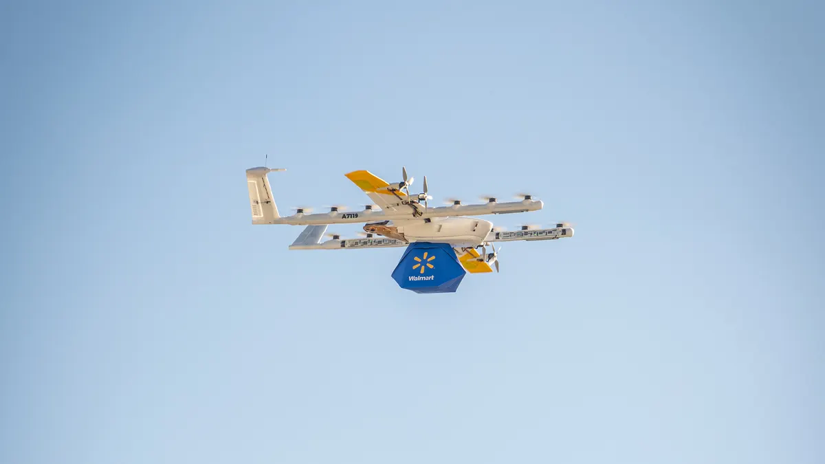 A drone in the sky carries a Walmart-branded package.