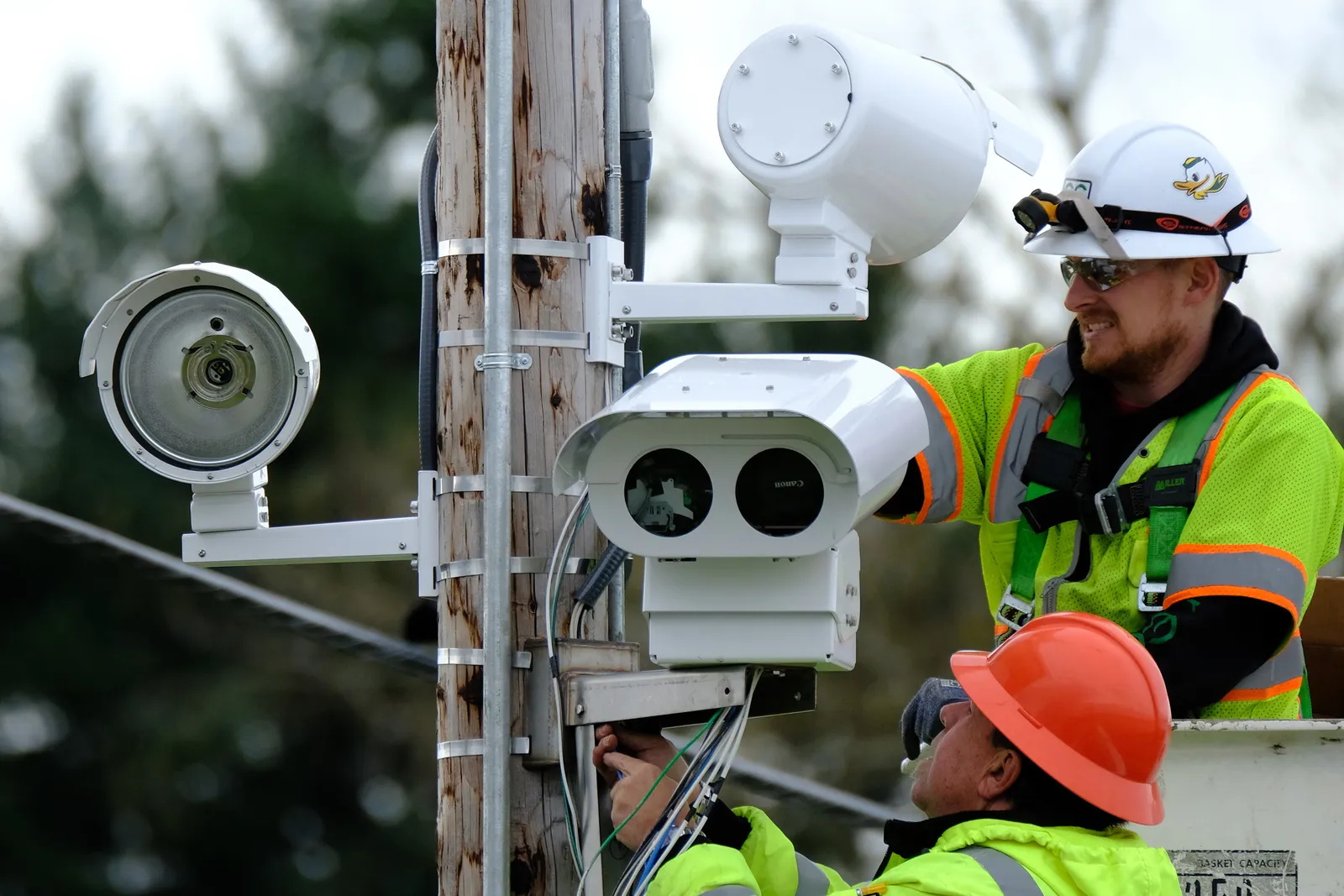 Two workers installing a speed safety camera on a utility pole.