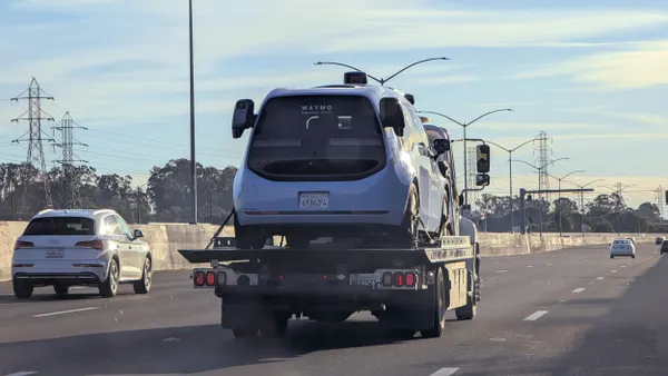 A blue vehicle on a flatbed truck along a highway with other cars.
