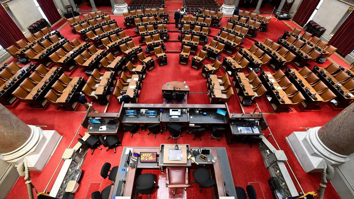 An overhead view of the New York state assembly chamber features a large podium with curved rows of seating. 