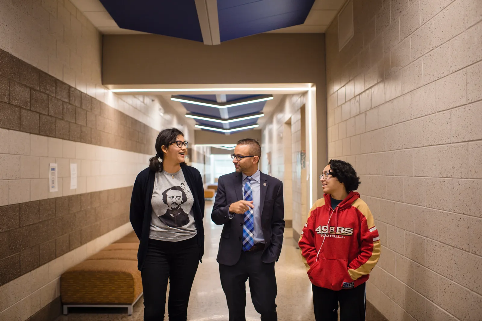 Adult stands with two secondary school students in a school building hallway. The people are looking at each other.