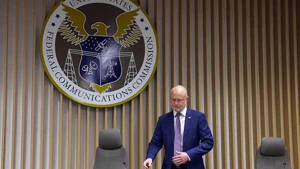 A man in a purple suit and tie sits in front of a federal emblem