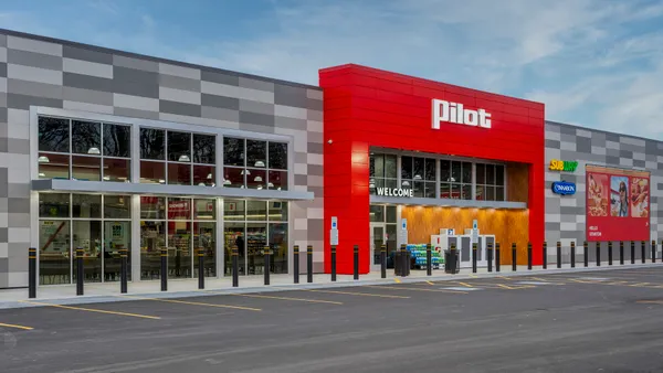 A photo of the exterior of a travel stop. Signs on the front wall of the gray and red building say "Pilot," Welcome," "Subway" and "Cinnabon."