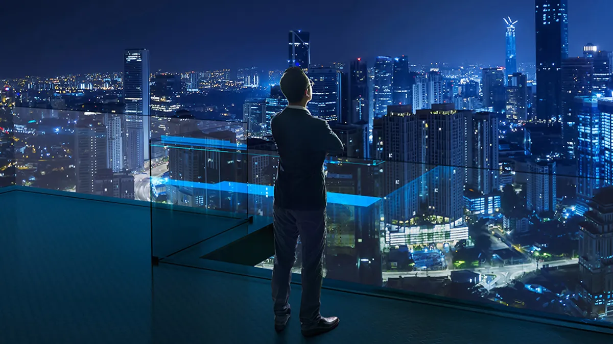 Businessman standing on open roof top balcony watching city night view