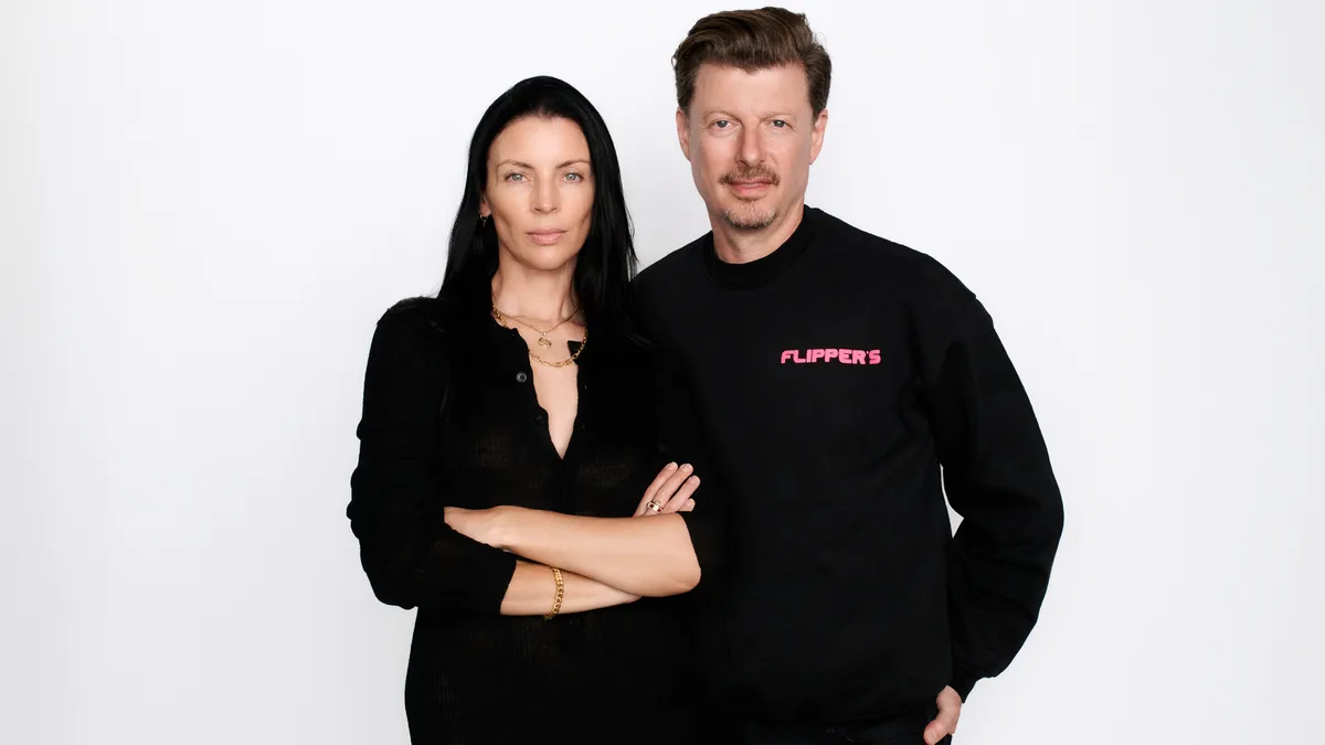 Two people stand side by side against a white background and stare at the camera.