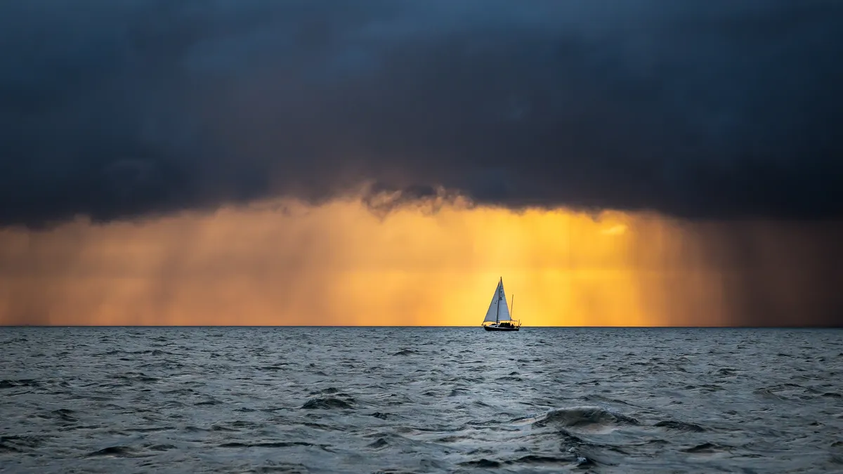 Lonely sailing yacht in the ocean at the approaching storm and raining clouds at sunrise