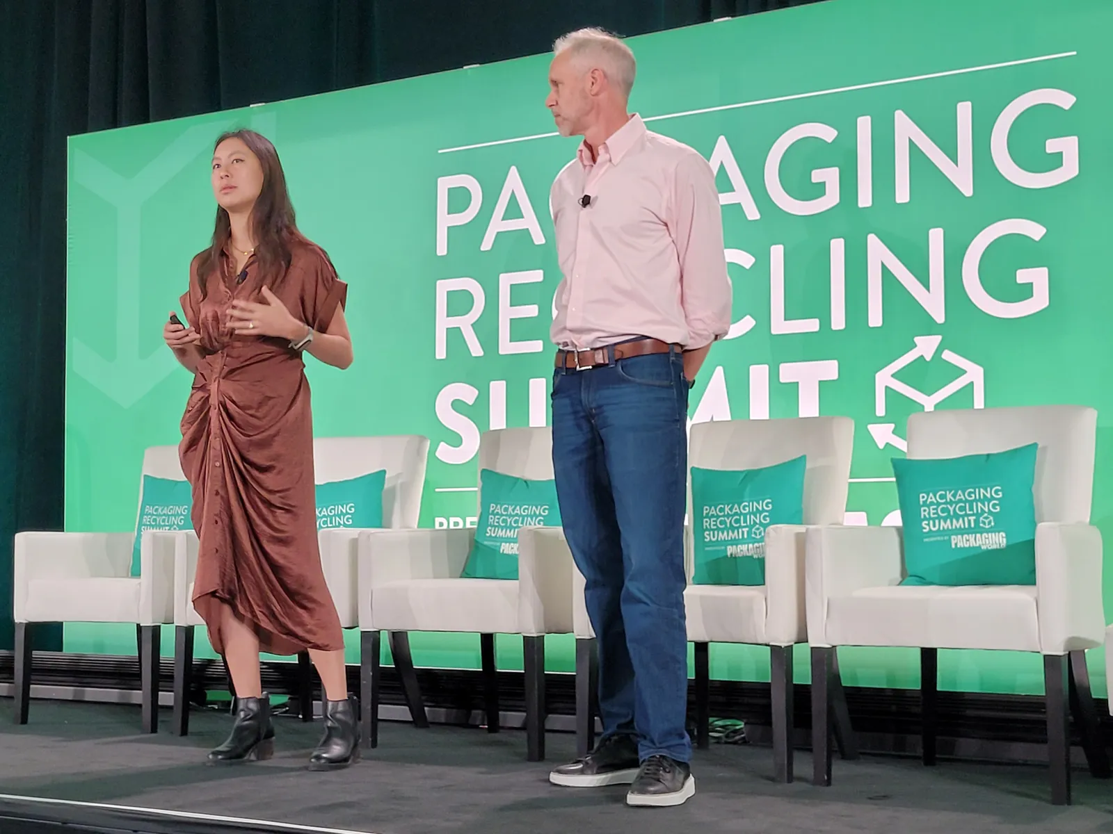 Two people stand on a stage at a conference with a green background behind them that says Packaging Recycling Summit.