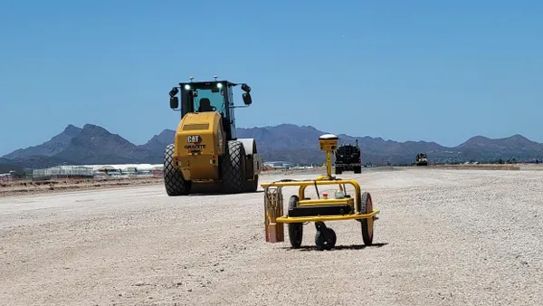 Two robots under a clear blue sky ride along on gravel.