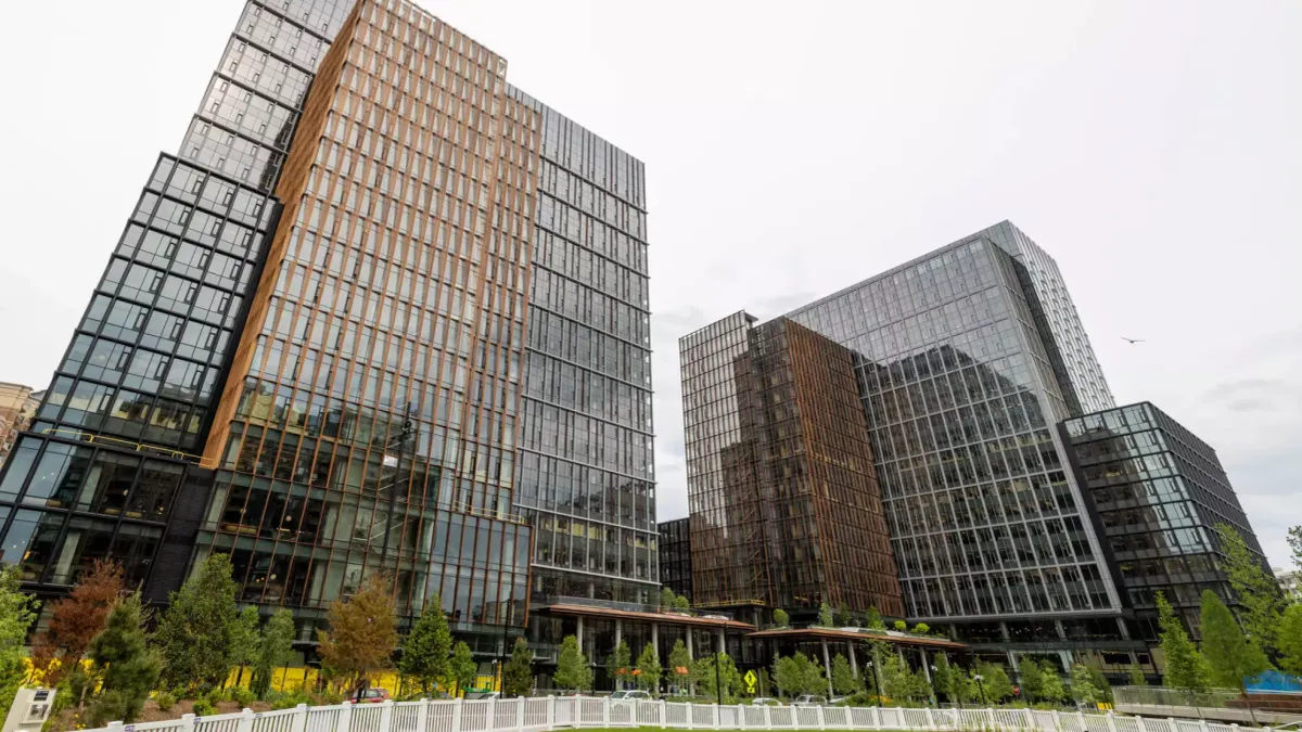 Two glass buildings loom in the foreground, with green grass and concrete sidewalks below them on a cloudy day.