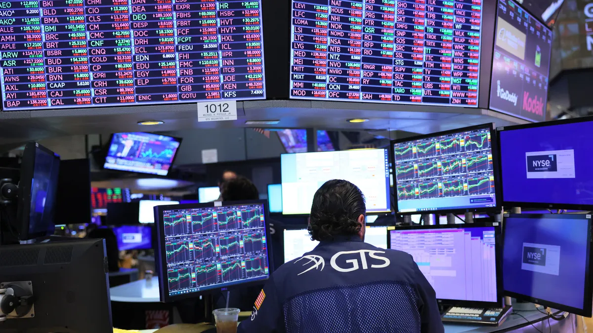 A trader sits at a computer in front of a wall of screens displaying stock informations at the New York Stock Exchange.