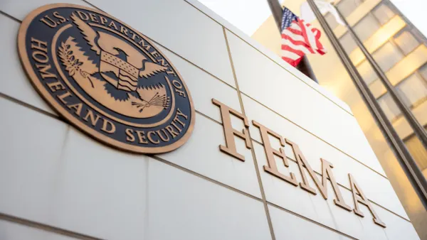 A wall of a stone building with the Department of Homeland Security seal and FEMA written on it with a U.S. flag in the background.