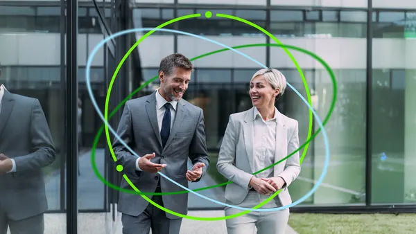 Two people in suits outside smiling with a Deloitte spherical illustration around them.