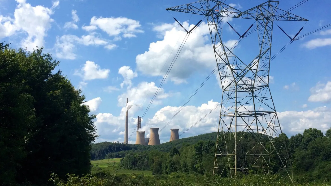 Electric transmission lines running through the woods to a power plant in the distance.